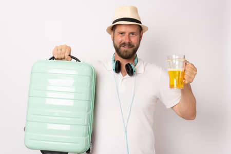 Young handsome man over isolated white background in vacation with travel suitcase and drinking beer