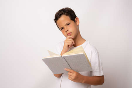 Happy thoughtful male student holding book isolated on a white backgroundの写真素材