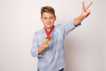 Young excited boy showing his golden medal with victory sign over white background.