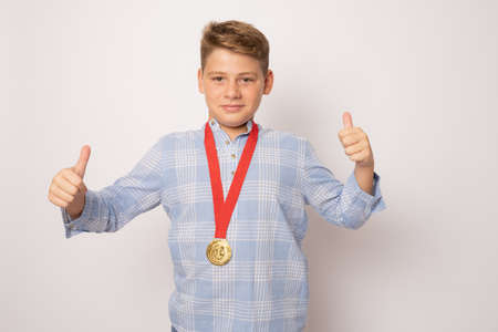 Young excited boy showing his golden medal with thumbs up over white background.の写真素材