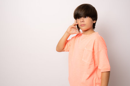 Child boy in casual t-shirt talking on the phone isolated over white background.の写真素材
