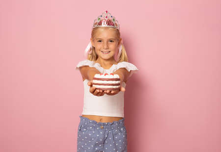 Cute little girl with princes crone and holding a cake isolated over pink background. Celebration birthday concept.の写真素材