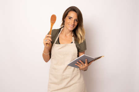 Smiling woman wearing apron holding kitchen utensils isolated over white background.の写真素材
