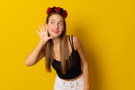 Young smiling woman in halloween costume making listening gesture isolated on yellow backgroundの写真素材