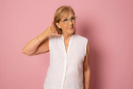 Smiling senior woman doing phone gesture with hand and fingers like talking on the telephone. Communicating concepts.の写真素材