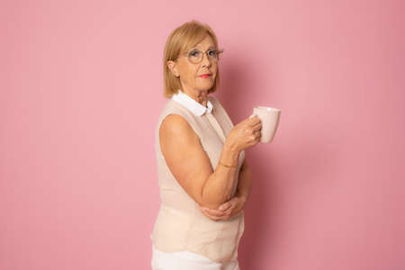 Senior beautiful woman drinking cup of coffee standing over isolated pink backgroundの写真素材