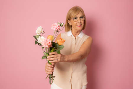 Close up photo of gorgeous lady holding bouquet of beautiful flowers in hands isolated pink backgroundの写真素材