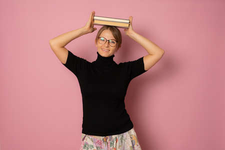 Photo of young beautiful smiling positive cheerful girl in glasses with pile of books isolated on pink color backgroundの写真素材