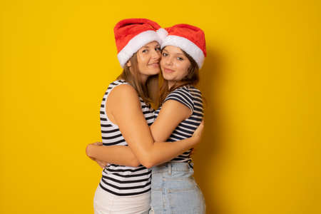 Happy mother and daughter together in santa hat over yellow background. Christmas concept.の写真素材