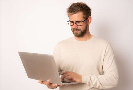 Studio portrait of a young smiling guy in a casual sweater with a laptop on a white backgroundの写真素材