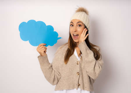 Young smiling woman in winter clothing holding paper cloud isolated over white background.の写真素材