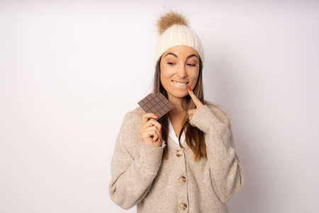 Beautiful young funny woman in winter clothing with chocolate bar on white backgroundの写真素材