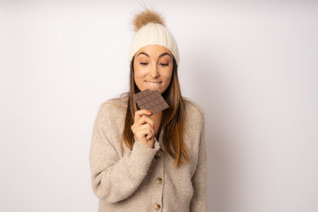 Portrait of a happy young woman biting chocolate bar isolated over white backgroundの写真素材