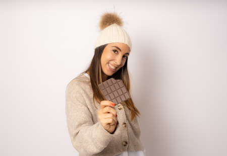Beautiful young happy woman in winter clothing with chocolate bar on white backgroundの写真素材