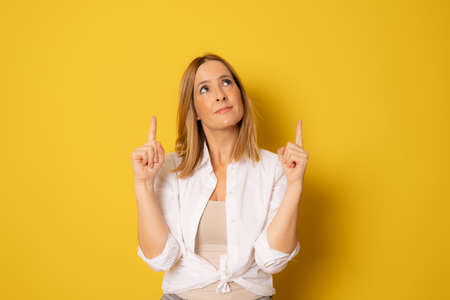 Portrait of beautiful young woman pointing up over yellow background.の写真素材