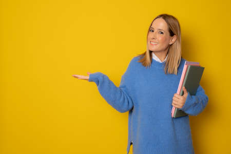 Portrait of happy young caucasian woman holding notebooks showing product with hand isolated on yellow backgroundの写真素材