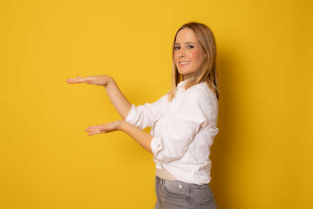 Young woman over isolated background holding something with both hands, product presentation.の写真素材