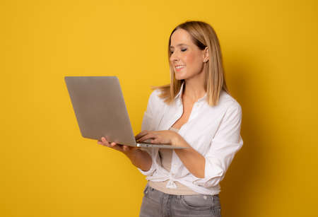 Image of cheerful young woman standing isolated over yellow background using laptop computer.の写真素材