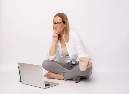 Business concept. Portrait of young woman in casual clothing sitting on floor in lotus pose and holding laptop isolated over white background.の写真素材