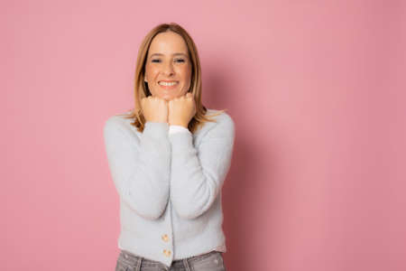 Young happy woman in winter sweater standing isolated over pink background.の写真素材