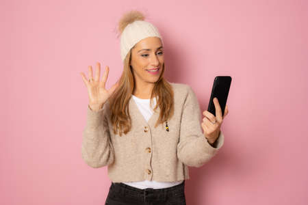 Young woman in winter clothing talking on mobile phone isolated over pink background.の写真素材