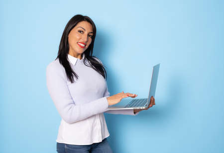 Image of cheerful young woman standing isolated over blue background using laptop computer. Looking camera.の写真素材