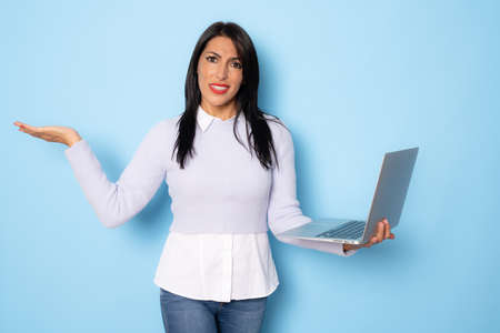Image of cheerful young woman standing isolated over blue background using laptop computer. Looking camera.の写真素材