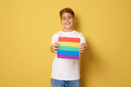 happy boy holding pop it game in hands, isolated on yellow background. Cheerful kid with pop itの写真素材