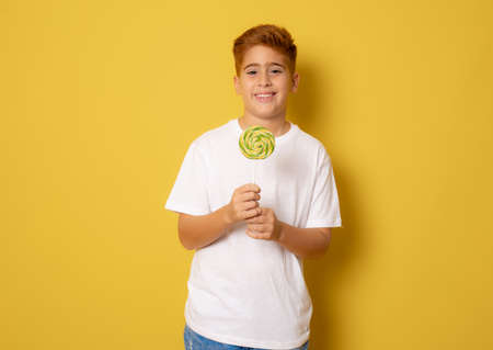 young boy with colorful lollipop isolated over yellow backgroundの写真素材