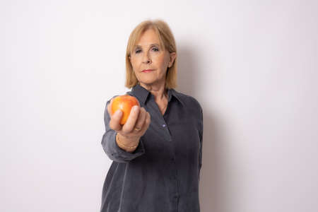 Portrait of a beautiful elderly woman holding an apple isolated over white background.の写真素材