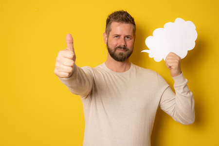 Young caucasian man isolated on yellow background holding an empty speech bubble with thumb upの写真素材