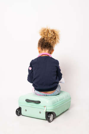 Back view little girl sitting on suitcase isolated over white background.の写真素材