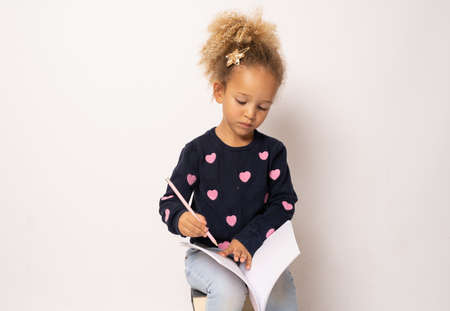 Little cute girl sitting on stack of books with a notebook. Isolated over white background.の写真素材
