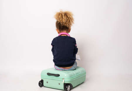 Back view little girl sitting on suitcase isolated over white background.の写真素材