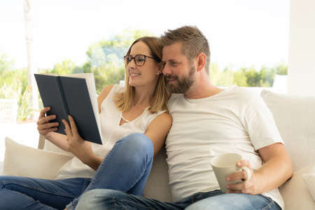 Spending nice time at home. Beautiful young loving couple bonding to each other and smiling while woman holding a bookの写真素材