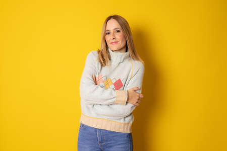 Young smiling woman in winter clothing with arms folded isolated over yellow background.の写真素材