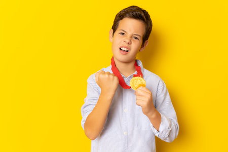 Cute child boy showing his gold medal isolated over yellow background.の写真素材