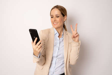 Young business woman using smartphone with victory sign isolated over white background.の写真素材