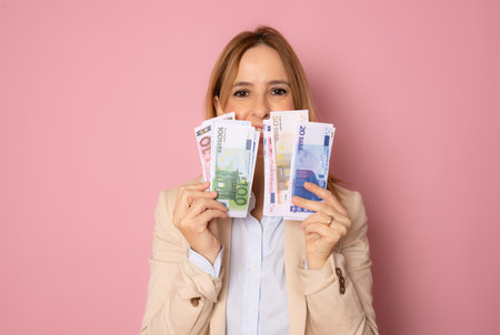 Photo of pretty smiling business woman standing isolated over pink background holding money.の写真素材