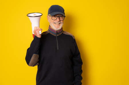 Mature man wearing cap holding megaphone isolated over yellow background.