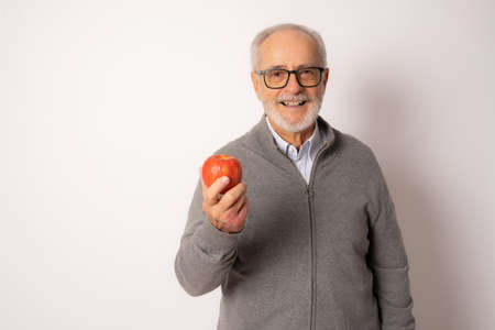 Senior happy man wearing casual sweater eating an apple isolated over white background.の写真素材