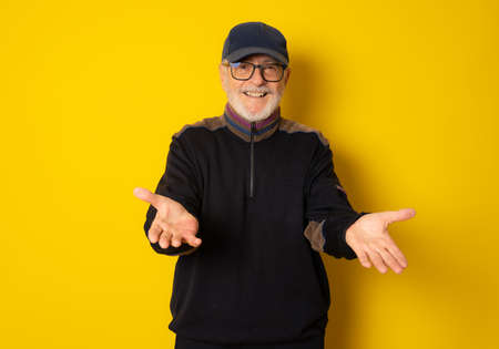 Mature smiling man in winter clothing showing product with hands isolated over yellow background.の写真素材