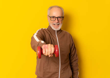 Happy mature sport man holding dumbbell isolated over yellow background.の写真素材