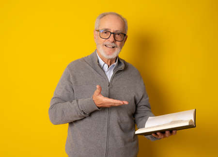 Mature smiling man reading a book isolated over yellow background.の写真素材