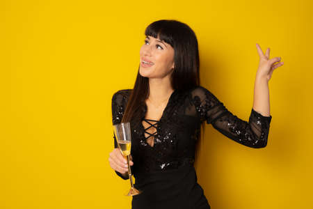 Young celebrating woman black dress . Beautiful model portrait isolated over yellow background hold wine glass.の写真素材