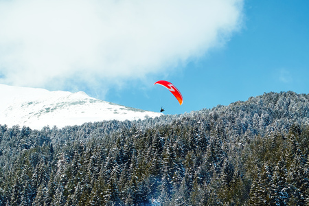 Landscape of mountains against the blue sky and white clouds. Forest of pine trees. Two paratroopers flying over the mountain massif against the blue skyの写真素材