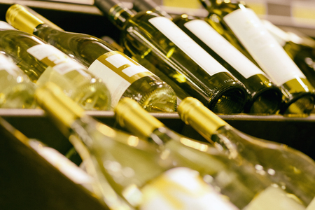 Blurred racks with bottles of white wine. Shelves with bottles of wine in a large grocery supermarket. Basic background for designの写真素材
