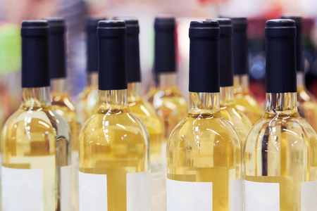 Blurred  bottles of white and rose wine are nicely laid out in a row on a shelf in a large supermarket. Bright abstract background ideal for any designの写真素材