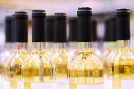 Blurred  bottles of white and rose wine are nicely laid out in a row on a shelf in a large supermarket. Bright abstract background ideal for any designの写真素材