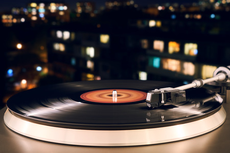 Turntable vinyl record player on the background of a sunset over the lights city. Sound technology...